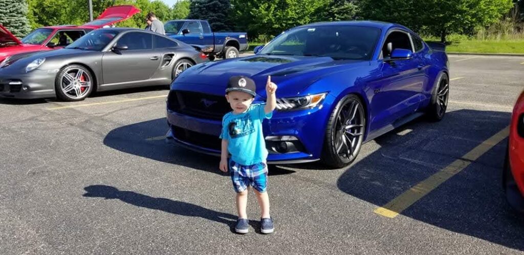 Young child standing in front of a blue car