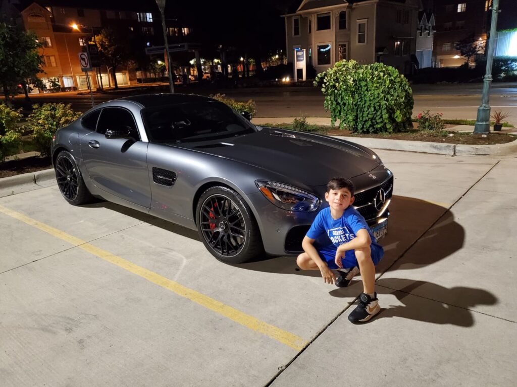 Young person crouching beside a dark sports car