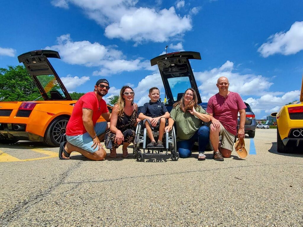 Group of adults and a child together between sports cars